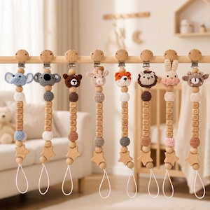 Könnte beinhalten: Eine Auswahl an personalisierten Schnullerhaltern für Babys. Jeder Halter hat einen gehäkelten Tierkopf, Holzperlen und einen Namen, der mit Holzbuchstaben aufgereiht ist. Die Halter haben einen sternförmigen Holzanhänger und eine Schlaufe.