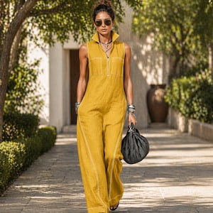 Könnte beinhalten: Ein ärmelloser, senfgelber Jumpsuit mit Kragen und Reißverschluss vorne. Der weitbeinige Jumpsuit hat weiße Nahtdetails und zwei Vordertaschen. Eine schwarz-weiß gestreifte Handtasche wird in der rechten Hand gehalten.