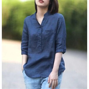 May include: A navy blue linen shirt with a mandarin collar and a small chest pocket. The shirt features three-quarter sleeves and a button-down placket. The shirt is worn with blue jeans.