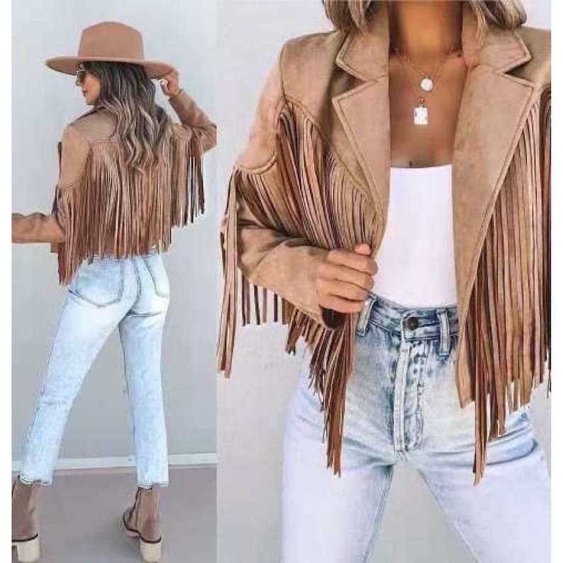 May include: A tan suede jacket with long fringe detailing on the sleeves and back. The jacket has a classic collar and is paired with light-wash jeans and a wide-brimmed hat. The outfit is a bohemian style.