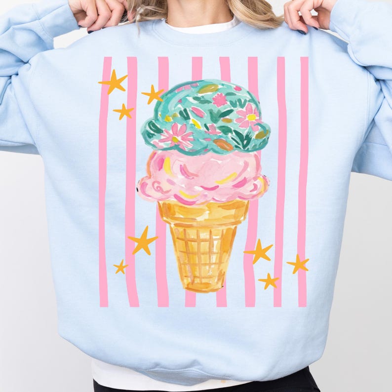 Retro pastel striped png featuring double scoop pastel ice cream cone top scoop has floral pattern and bottom scoop is pink.  Background stripes are pink yellow stars scattered.   Shown here on a blue sweatshirt.