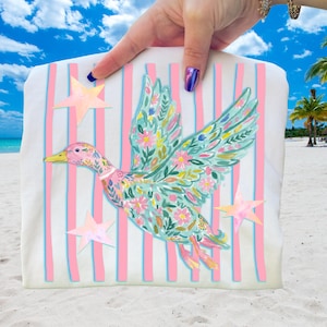 May include: White tote bag with a colorful duck illustration. The duck has floral and leaf details in its wings and body. Pink and blue stripes are on the background, with three pink stars.