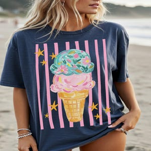 Retro pastel striped png featuring double scoop pastel ice cream cone top scoop has floral pattern and bottom scoop is pink.  Background stripes are pink yellow stars scattered.   Shown here on woman at the beach wearing a navy tee.