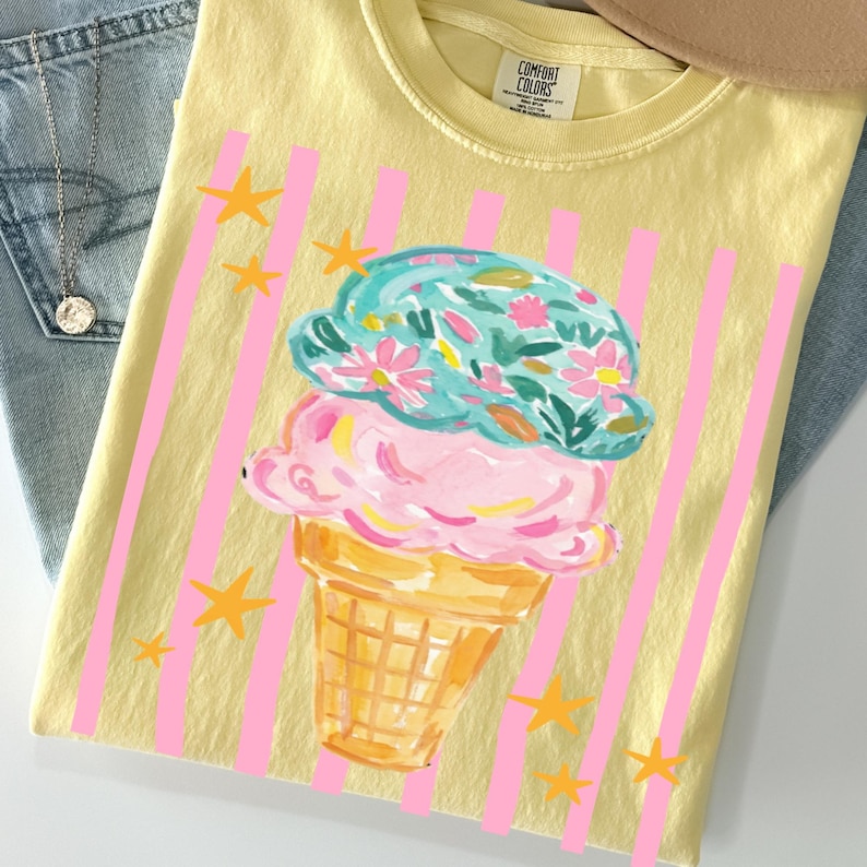 Retro pastel striped png featuring double scoop pastel ice cream cone top scoop has floral pattern and bottom scoop is pink.  Background stripes are pink yellow stars scattered.   Shown here on a folded butter tee.