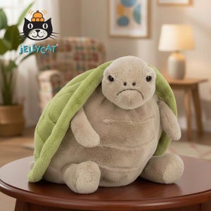 May include: A plush turtle toy with a grumpy expression. The turtle has a light green shell and a beige body. The toy is sitting on a wooden table. The Jellycat logo is in the upper left corner.