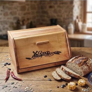 May include: A wooden bread box with a hinged lid and a handle, alongside a loaf of sliced bread. The box has the word "Bread" etched on the front. Red chili peppers, olives, and corn are scattered on the wooden surface.