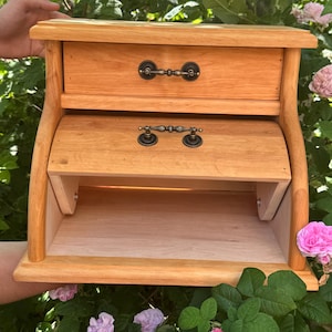 Peut inclure: Une boîte à pain en bois brun clair dotée d'un tiroir supérieur avec une poignée en métal foncé et d'un compartiment inférieur avec une porte abattante comprenant également une poignée en métal foncé assortie. Structure en bois naturel.