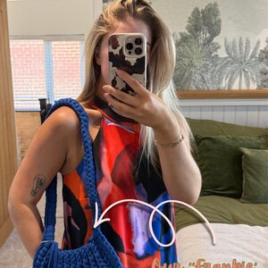May include: Cobalt blue Frankie bag with a braided strap and fringe detail. The bag is made of a thick, textured material. The image also shows a colorful dress.
