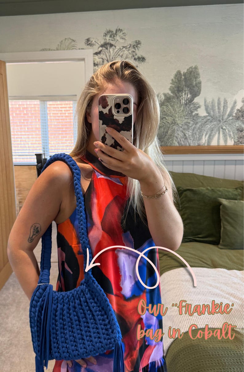 May include: Cobalt blue Frankie bag with a braided strap and fringe detail. The bag is made of a thick, textured material. The image also shows a colorful dress.