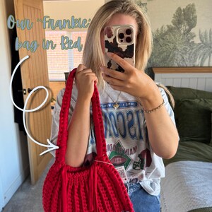 May include: A red Frankie bag with a woven design and long handles. The bag has a rounded shape with fringe detailing. The text "Our Frankie bag in Red" is visible in the image. The bag is held by a person.
