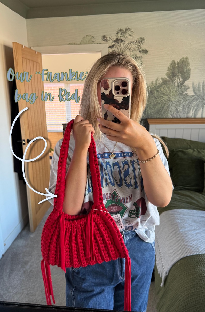 May include: A red Frankie bag with a woven design and long handles. The bag has a rounded shape with fringe detailing. The text "Our Frankie bag in Red" is visible in the image. The bag is held by a person.