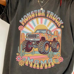 Comfort Colors graphic tee featuring a retro groovy monster truck with floral details, desert cacti, and a sunburst backdrop, arched text reading Monster Truck Mama, designed for moms of boys, Monster Jam fans, and birthday party season.