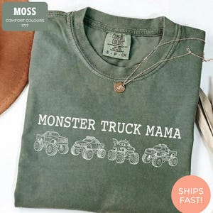 Moss Comfort Colors t-shirt featuring the text "MONSTER TRUCK MAMA" and four white monster truck designs. The shirt has a crew neck and short sleeves.