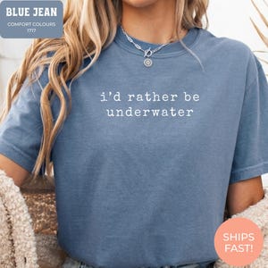 May include: A blue jean coloured t-shirt with the phrase "i'd rather be underwater" in white text. The shirt is a Comfort Colours 1717 style. The top is a short-sleeved shirt.