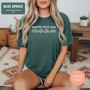 Blue Spruce Comfort Colors t-shirt featuring the text "MONSTER TRUCK MAMA" and four white monster truck designs. The shirt has a crew neck and short sleeves.