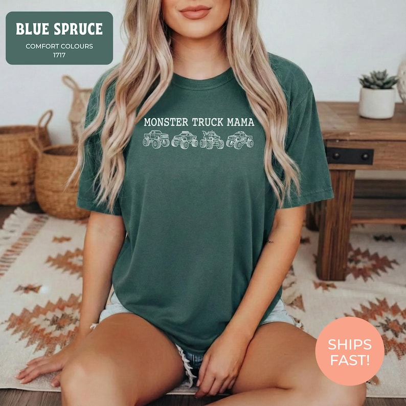 Blue Spruce Comfort Colors t-shirt featuring the text "MONSTER TRUCK MAMA" and four white monster truck designs. The shirt has a crew neck and short sleeves.