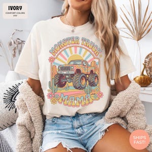 Comfort Colors graphic tee featuring a retro groovy monster truck with floral details, desert cacti, and a sunburst backdrop, arched text reading Monster Truck Mama, designed for moms of boys, Monster Jam fans, and birthday party season.