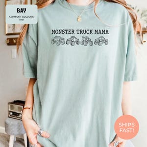Bay Comfort Colors t-shirt featuring the text "MONSTER TRUCK MAMA" and four black monster truck designs. The shirt has a crew neck and short sleeves.