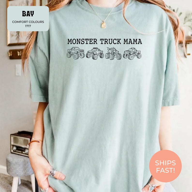 Bay Comfort Colors t-shirt featuring the text "MONSTER TRUCK MAMA" and four black monster truck designs. The shirt has a crew neck and short sleeves.