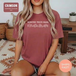 Crimson Comfort Colors t-shirt featuring the text "MONSTER TRUCK MAMA" and four white monster truck designs. The shirt has a crew neck and short sleeves.