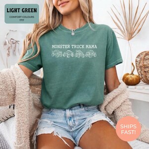 Light Green Comfort Colors t-shirt featuring the text "MONSTER TRUCK MAMA" and four white monster truck designs. The shirt has a crew neck and short sleeves.