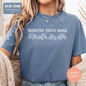 Blue Jean Comfort Colors t-shirt featuring the text "MONSTER TRUCK MAMA" and four white monster truck designs. The shirt has a crew neck and short sleeves.