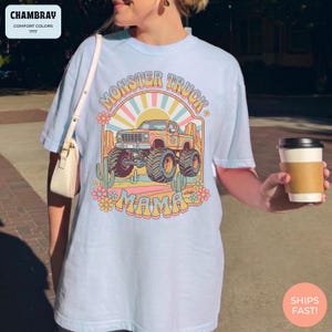 Comfort Colors graphic tee featuring a retro groovy monster truck with floral details, desert cacti, and a sunburst backdrop, arched text reading Monster Truck Mama, designed for moms of boys, Monster Jam fans, and birthday party season.