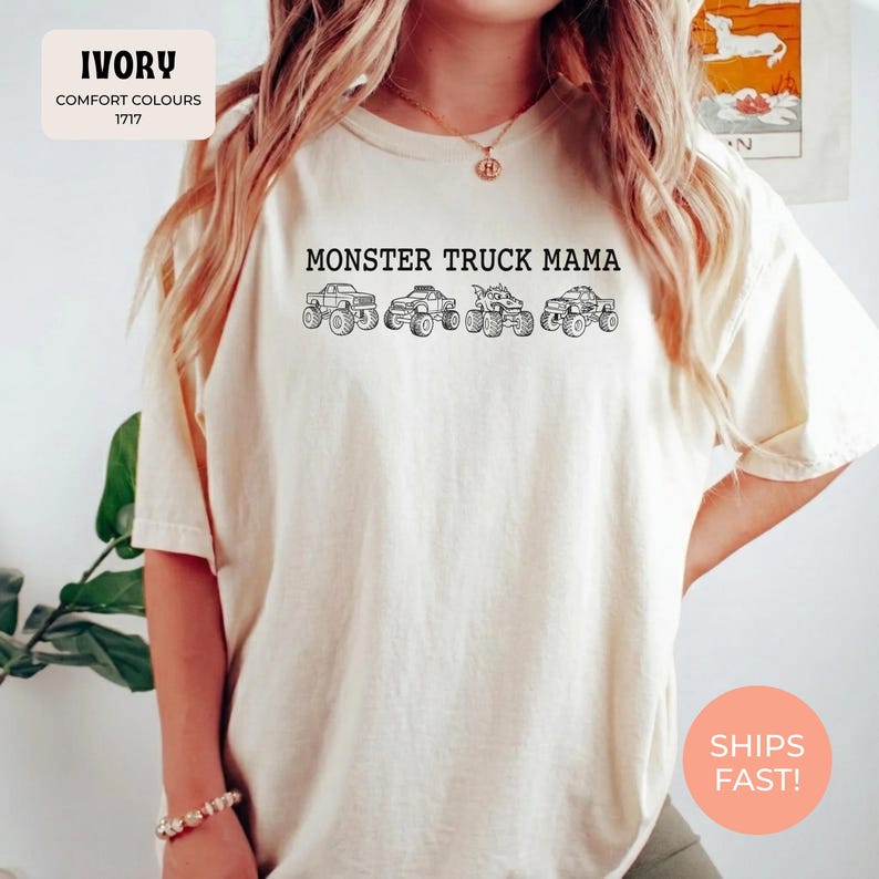Ivory Comfort Colors t-shirt featuring the text "MONSTER TRUCK MAMA" and four white monster truck designs. The shirt has a crew neck and short sleeves.