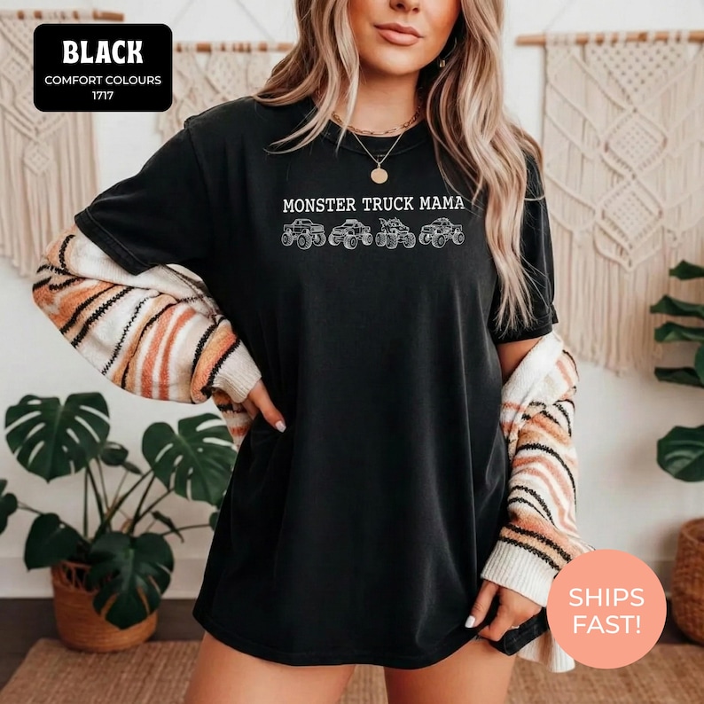 Black Comfort Colors t-shirt featuring the text "MONSTER TRUCK MAMA" and four white monster truck designs. The shirt has a crew neck and short sleeves.