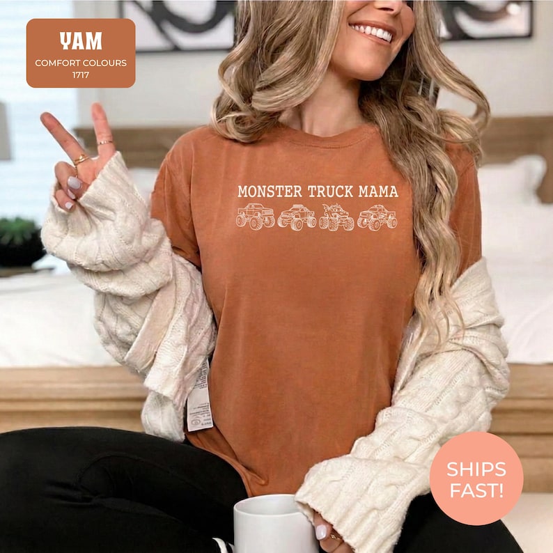 Yam Comfort Colors t-shirt featuring the text "MONSTER TRUCK MAMA" and four white monster truck designs. The shirt has a crew neck and short sleeves.
