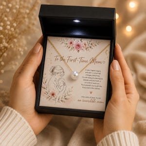 May include: A gold chain necklace with a single white pearl pendant presented in a black gift box. The box insert features a floral illustration, a drawing of a mother and baby, and the text To the First-Time Mom and You are going to be an incredible mom.