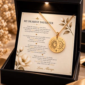 May include: A gold-toned circular pendant necklace featuring an engraved sun and moon design, presented on a cream-coloured card with the text MY DEAREST DAUGHTER and a heartfelt message, all housed inside a black gift box with integrated lighting.