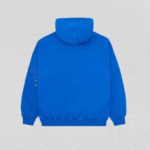 K&ouml;nnte beinhalten: Ein leuchtend blauer Kapuzenpullover mit Kapuze und langen &Auml;rmeln. Der linke &Auml;rmel hat bunte, gestickte Stern- und Punktmuster. Der Kapuzenpullover ist aus weichem Material und f&uuml;r den Freizeitgebrauch geeignet.