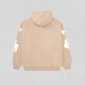 K&ouml;nnte beinhalten: Ein beigefarbener Kapuzenpullover mit Kapuze und langen &Auml;rmeln. Auf den &Auml;rmeln sind wei&szlig;e, abstrakte Formen aufgedruckt. Der Hoodie besteht aus einem weichen Material und eignet sich f&uuml;r den l&auml;ssigen Gebrauch.