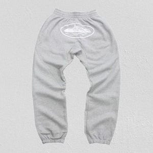Op de afbeelding: Lichtgrijze joggingbroek met een elastische tailleband en manchetten. Een witte ovale afbeelding is gecentreerd op de rug, met een lijntekening van een vuurtoren en eiland. De broek is gemaakt van een zacht, comfortabel materiaal.