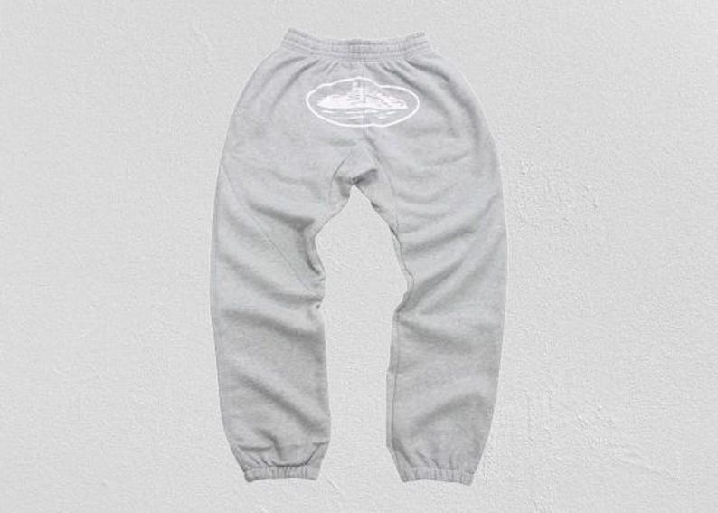 Op de afbeelding: Lichtgrijze joggingbroek met een elastische tailleband en manchetten. Een witte ovale afbeelding is gecentreerd op de rug, met een lijntekening van een vuurtoren en eiland. De broek is gemaakt van een zacht, comfortabel materiaal.