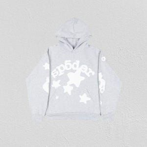 K&ouml;nnte beinhalten: Ein hellgrauer Kapuzenpullover mit Kapuze und K&auml;ngurutasche. Auf der Vorderseite steht das Wort "sp5der" in wei&szlig;er, stilisierter Schrift, zusammen mit wei&szlig;en Sternen. Die &Auml;rmel haben ebenfalls wei&szlig;e Grafiken. Der Hoodie ist aus weichem Material.
