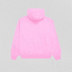 K&ouml;nnte beinhalten: Ein hellrosa Kapuzenpullover mit Kordelzug und langen &Auml;rmeln. Die &Auml;rmel sind mit kleinen, bunten Farbspritzern verziert. Der Hoodie besteht aus einem weichen Material und ist f&uuml;r den Alltag geeignet.