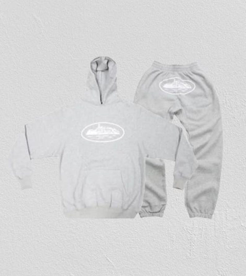 Op de afbeelding: Een lichtgrijze hoodie en joggingbroek set. De hoodie heeft een voorzak en een capuchon. Beide stukken hebben een wit ovaal ontwerp met een landschapsafbeelding. De joggingbroek heeft een elastische tailleband en manchetten.