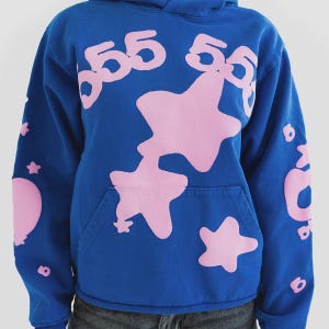 K&ouml;nnte beinhalten: Blauer Kapuzenpullover mit rosa Sternen und der Zahl 55. Der Hoodie hat eine K&auml;ngurutasche und eine Kapuze mit Kordelzug. Zus&auml;tzliche rosa Grafiken befinden sich auf den &Auml;rmeln. Das Design ist verspielt und auff&auml;llig.