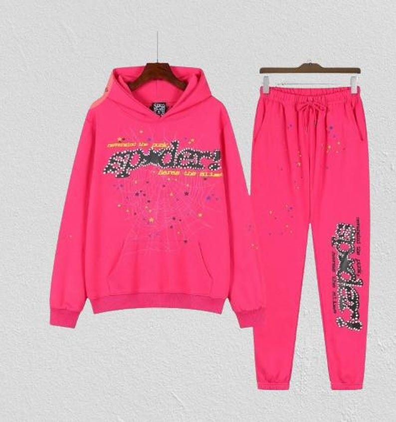 Puede incluir: Un conjunto de ch&aacute;ndal rosa brillante que consta de una sudadera con capucha y pantalones a juego. Tanto la sudadera con capucha como los pantalones muestran la palabra "SPYDER" en una fuente estilizada. Un conjunto llamativo.