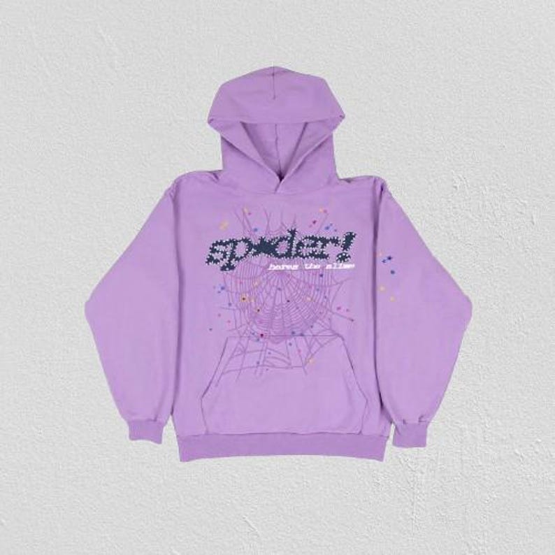 K&ouml;nnte beinhalten: Ein lila Kapuzenpullover mit einem Spinnennetz-Design und dem Wort "spider!" in einer pixeligen Schriftart. Der Hoodie hat eine K&auml;ngurutasche und eine Kapuze mit Kordelzug. Die Grafik enth&auml;lt bunte Punkte.