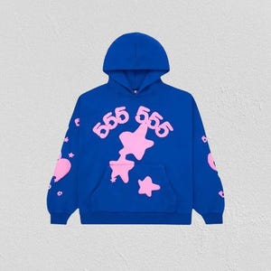 K&ouml;nnte beinhalten: Ein k&ouml;nigsblauer Hoodie mit einer Vordertasche und einer Kapuze. Der Hoodie hat rosa Stern- und Herzgrafiken sowie die Zahl "555" in einer stilisierten Schriftart. Das Design wiederholt sich auf den &Auml;rmeln.
