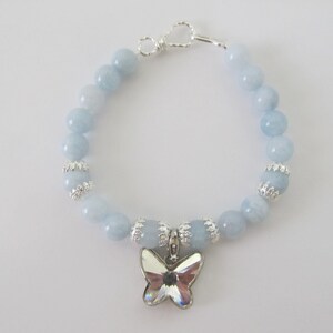 May include: A light blue beaded bracelet with a silver butterfly charm. The bracelet features round, light blue beads and silver accents. The butterfly charm is made of clear crystals and silver metal.
