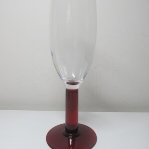 May include: A clear glass champagne flute with a deep red stem and base.