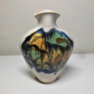 Può includere: Un vaso in ceramica bianca con un designo astratto unico. Il vaso presenta un motivo a spirale di smalto blu, verde e marrone.