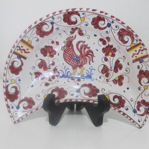 Puede incluir: Un plato de servir de cerámica blanco en forma de media luna con un diseño de gallo rojo y patrones florales en rojo, amarillo y azul.
