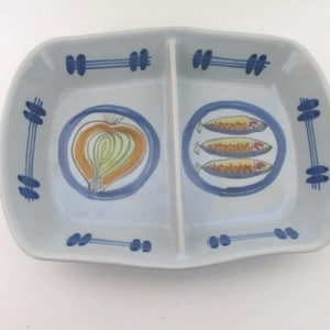 May include: A divided ceramic serving dish with a light blue background. The dish features a hand-painted design with a half onion and three fish in blue circles. Blue and white geometric shapes decorate the edges.