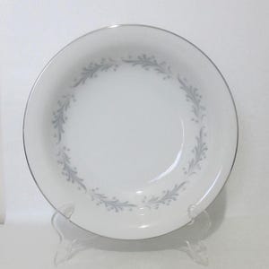 May include: A white ceramic bowl with a silver rim and a gray floral design around the edge.
