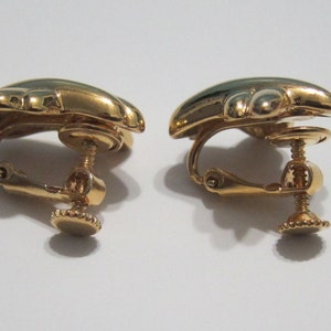 May include: A pair of gold-coloured clip-on earrings. Each earring has a rounded, beetle-shaped design with a dark green enamel centre. The clip-on mechanism includes a screw adjustment for a secure fit.